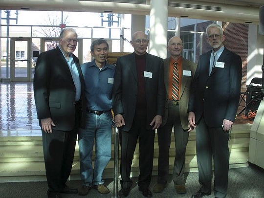 Five individuals "CS department founders" in formal attire with name tags standing indoors in front of large windows