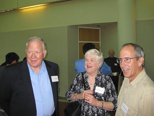 hree individuals with name tags in a social setting, with other people and a column visible in the background