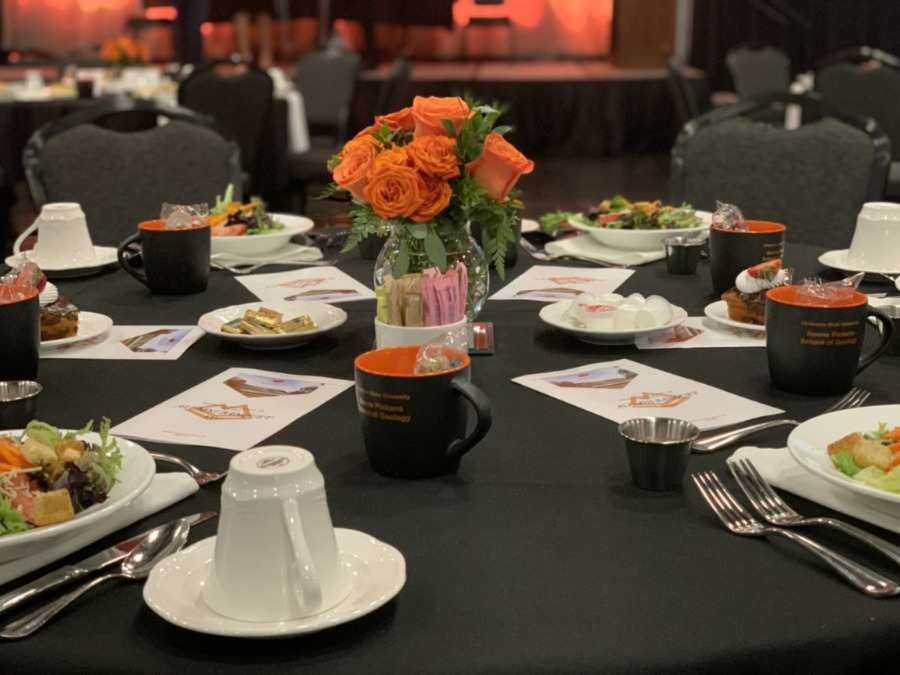 Banquet table set up with plates of salad and programs along with a orange roses as a center piece. Banquet table set up with plates of salad and programs along with a orange roses as a center piece.