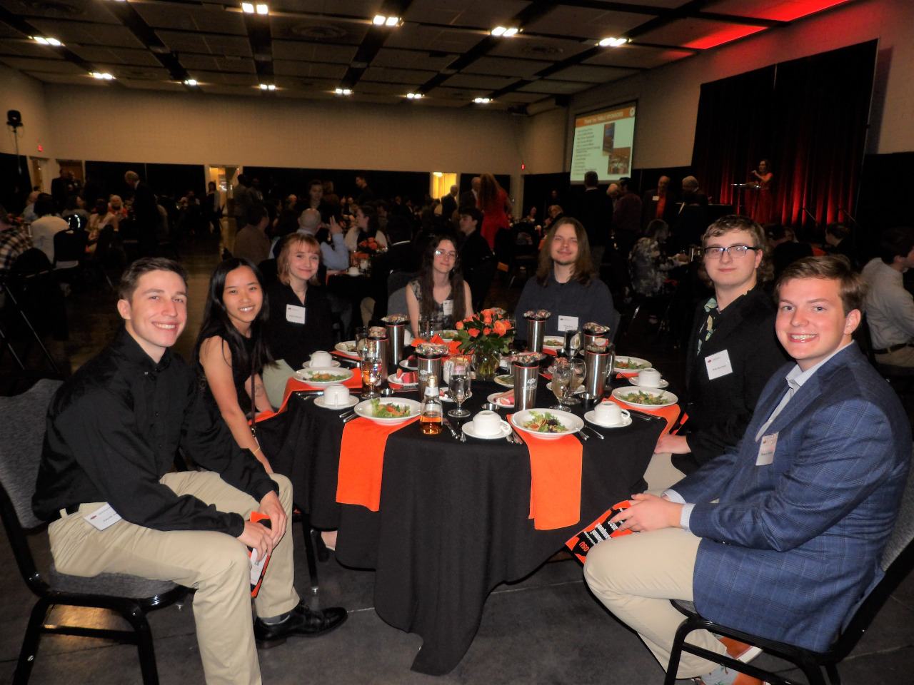 Four male and three female students sitting down enjoying the banquet dinner. Four male and three female students sitting down enjoying the banquet dinner.