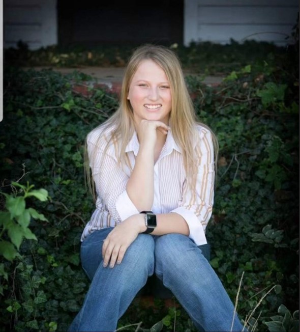 A woman with blonde hair poses in front of a natural background.