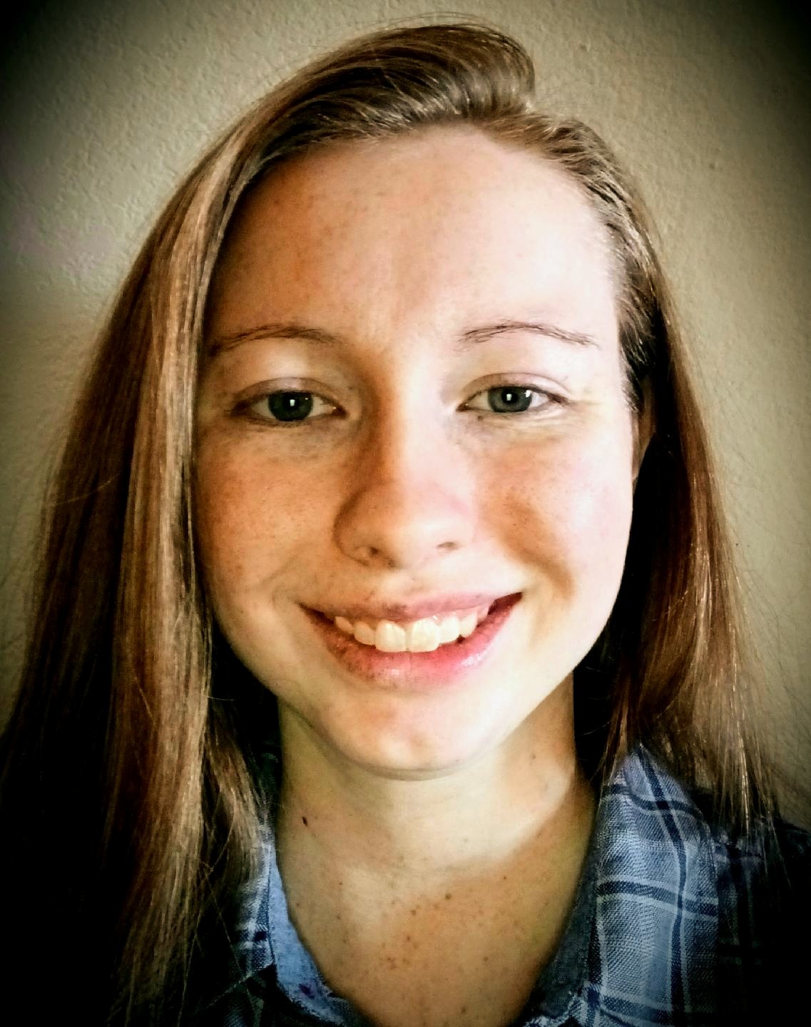 A headshot of a woman with long blonde hair and green shirt stand against a neutral backdrop.