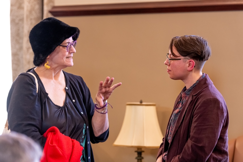 Doyle speaking with a bespectacled woman wearing a large hat