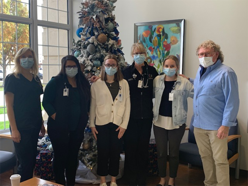 Group students with masks on in front of a Christmas tree looking at camera