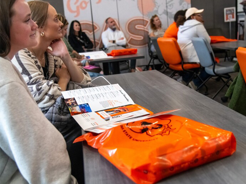Prospective students sitting at a table, listening to the recruiter, with their goody bags placed in front of them.