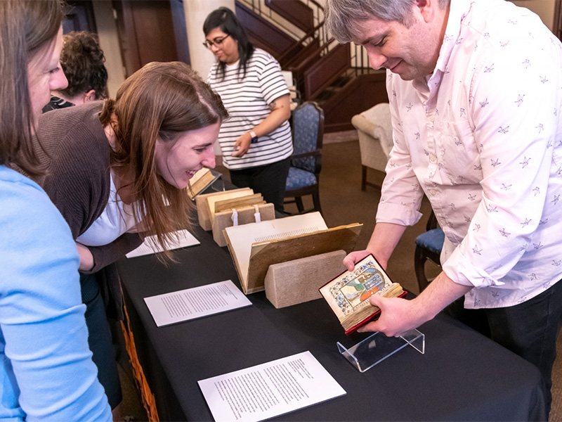 Students gathered around a table, paying attention to a presentation on a medieval manuscript.
