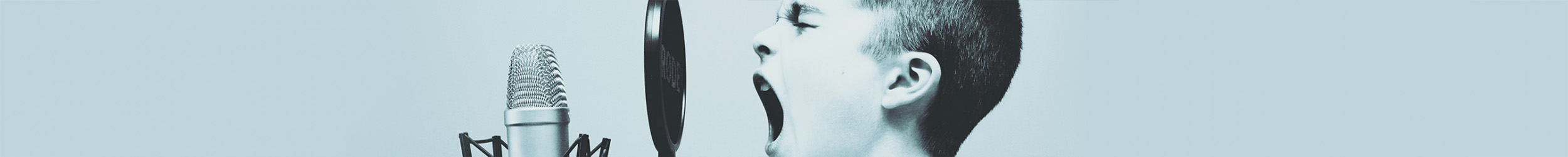 Close-up of a young man passionately yelling or singing behind a microphone, with a solid color background.