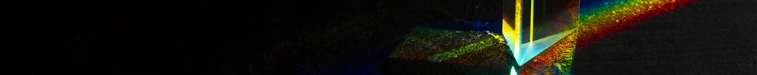 Light passing through glass, forming a rainbow of colors against a dark background.